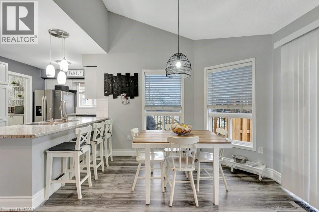 Open-concept kitchen and dining area featuring wood-finish flooring, a kitchen island with stone countertop, stainless steel appliances, and multiple windows - 49 Small Court, Cambridge, ON - Indoor Photo Showing Dining Room