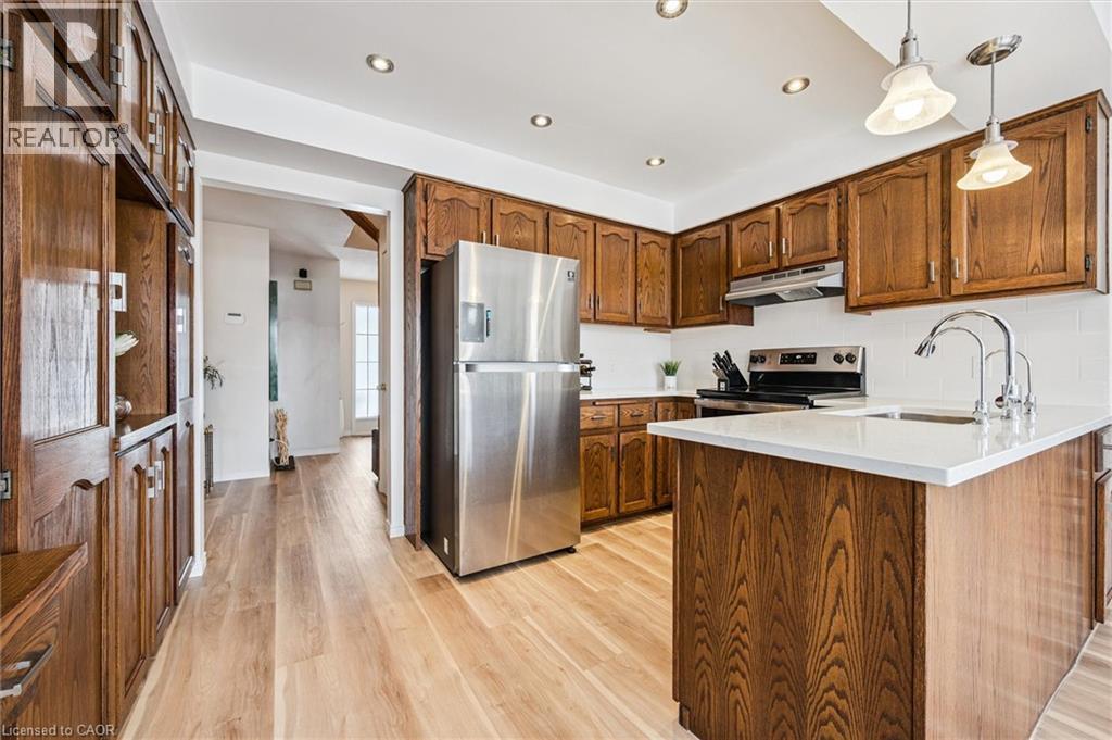 Kitchen featuring wood-finish cabinetry, stainless steel appliances, a white subway tile backsplash, and a central island with a white countertop and double basin sink - 488 Heather Hill Place, Waterloo, ON - Indoor Photo Showing Kitchen