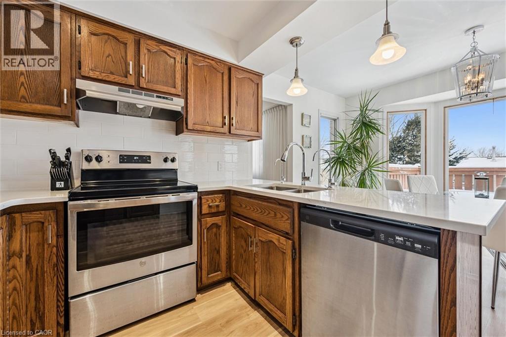 Well-appointed kitchen featuring wood cabinetry, stainless steel appliances, crisp white subway tile backsplash, light-toned countertops, and wood-finish flooring - 488 Heather Hill Place, Waterloo, ON - Indoor Photo Showing Kitchen With Stainless Steel Kitchen With Double Sink