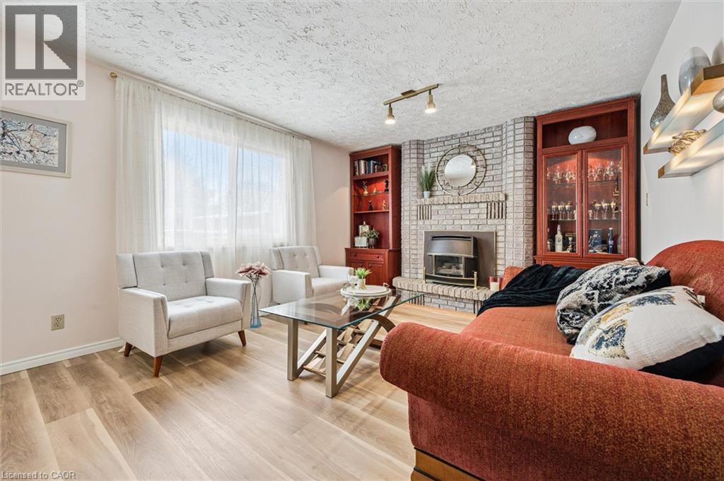 Spacious living area featuring light wood-finish flooring, a prominent brick-clad fireplace with a metal insert, and built-in wood cabinetry with glass display doors - 488 Heather Hill Place, Waterloo, ON - Indoor Photo Showing Living Room With Fireplace
