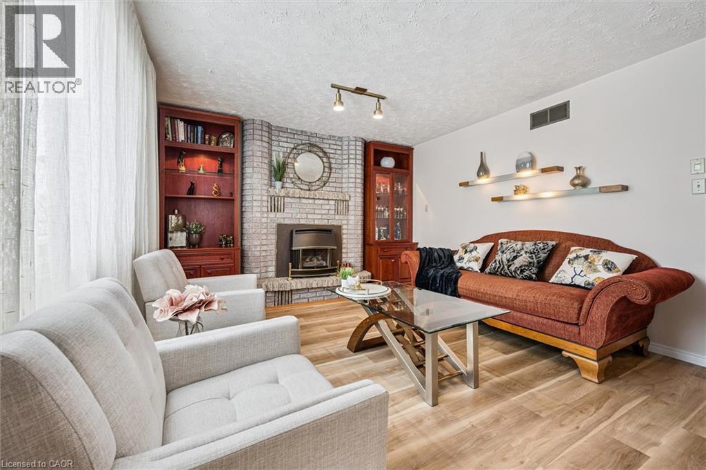 Living area featuring wood-finish flooring, a brick fireplace with a built-in firebox, a built-in corner bookcase, an additional built-in cabinet with glass doors, and wall-mounted display shelves - 488 Heather Hill Place, Waterloo, ON - Indoor Photo Showing Living Room With Fireplace