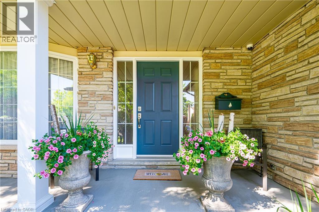 Inviting front entry featuring a deep blue door with sidelights, stacked stone facade, sheltered porch, and a column accent - 488 Heather Hill Place, Waterloo, ON - Outdoor With Deck Patio Veranda With Exterior