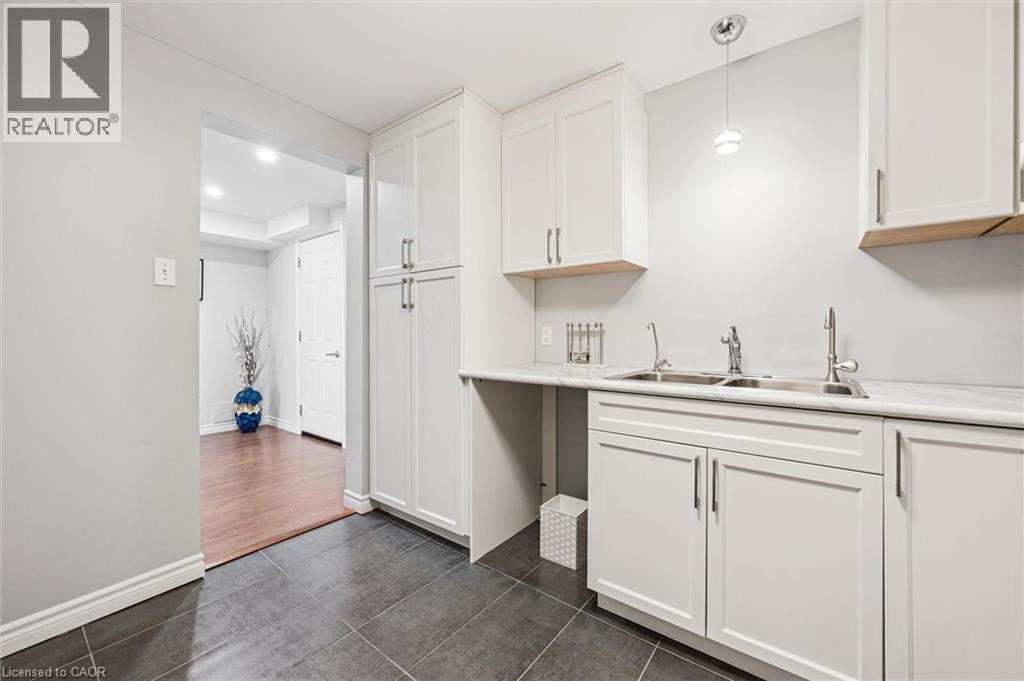 Kitchenette featuring white cabinetry, a dual stainless steel sink, light-toned countertop, and dark-toned floor tiles - 488 Heather Hill Place, Waterloo, ON - Indoor Photo Showing Kitchen With Double Sink
