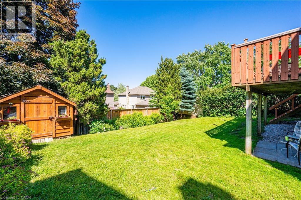 Expansive backyard featuring a lush green lawn, mature trees, a wood storage shed, and a raised wood deck with privacy railing - 488 Heather Hill Place, Waterloo, ON - Outdoor With Deck Patio Veranda
