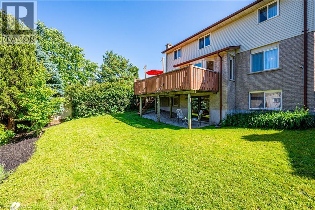 Expansive backyard featuring a lush lawn, established perimeter trees, and a raised wooden deck with railings - 488 Heather Hill Place, Waterloo, ON - Outdoor With Deck Patio Veranda