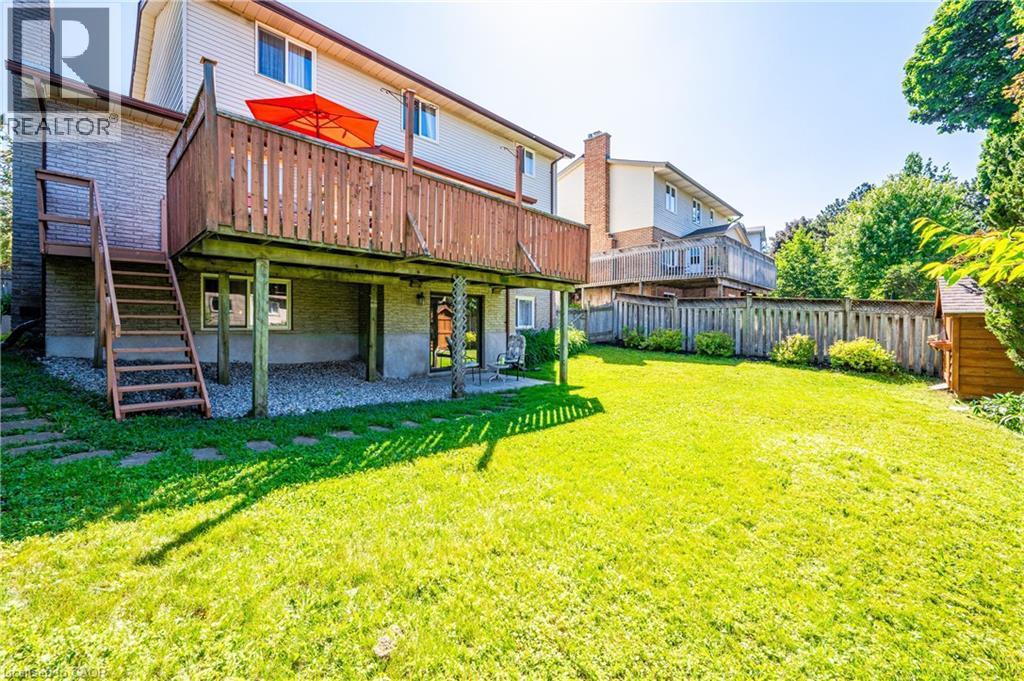 Spacious rear yard featuring an expansive lawn, a raised wood deck with staircase access, and a lower-level gravel patio - 488 Heather Hill Place, Waterloo, ON - Outdoor With Deck Patio Veranda
