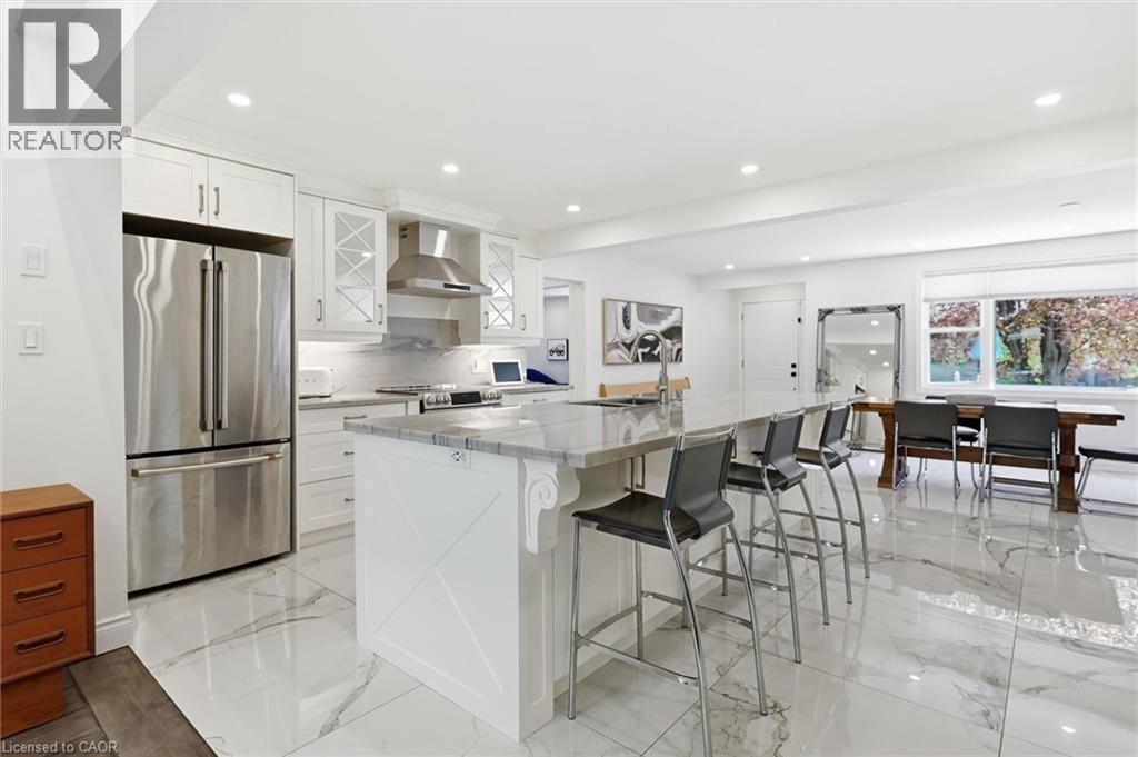 Open-concept kitchen featuring white shaker cabinetry, stainless steel appliances, a large island with seating, and polished marble-look flooring - 24 Glenwood Crescent, Hamilton, ON - Indoor Photo Showing Kitchen With Upgraded Kitchen
