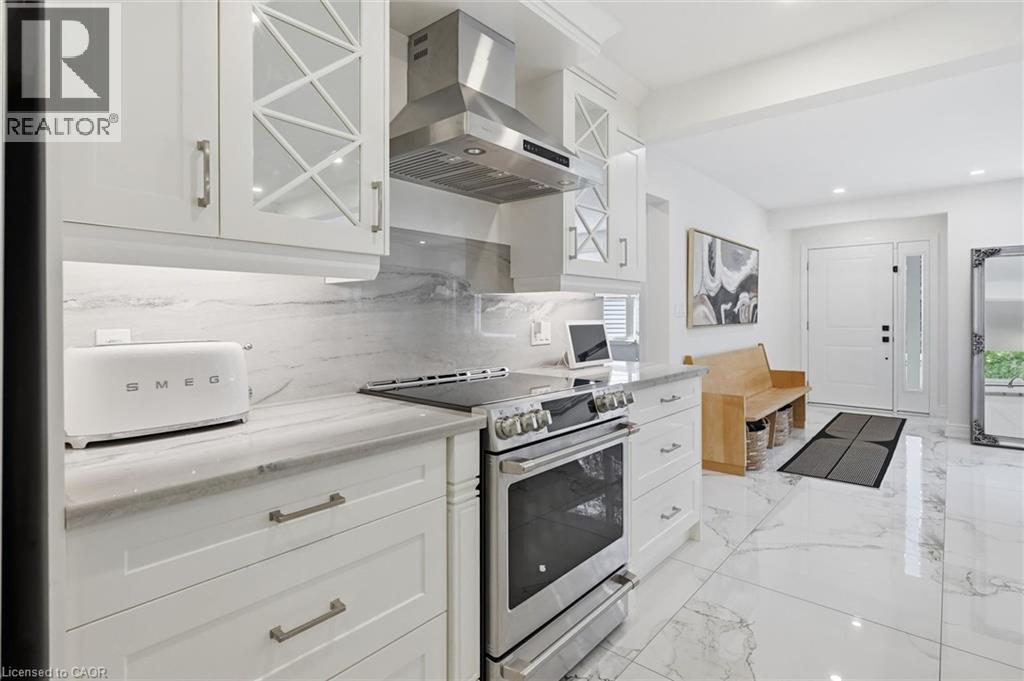 White cabinetry with glass-front accents, stainless steel appliances, marble-look countertops, matching backsplash, and marble-look flooring - 24 Glenwood Crescent, Hamilton, ON - Indoor Photo Showing Kitchen