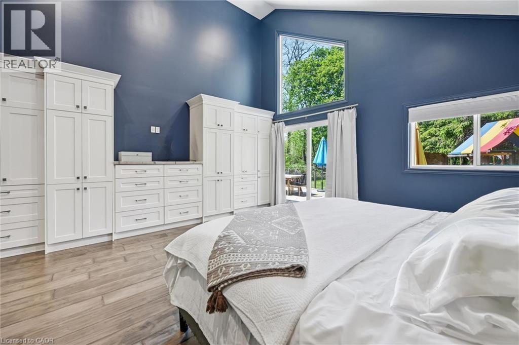 Vaulted ceiling room featuring extensive white built-in cabinetry with silver-tone hardware, wood-finish flooring, and multiple window exposures - 24 Glenwood Crescent, Hamilton, ON - Indoor Photo Showing Bedroom