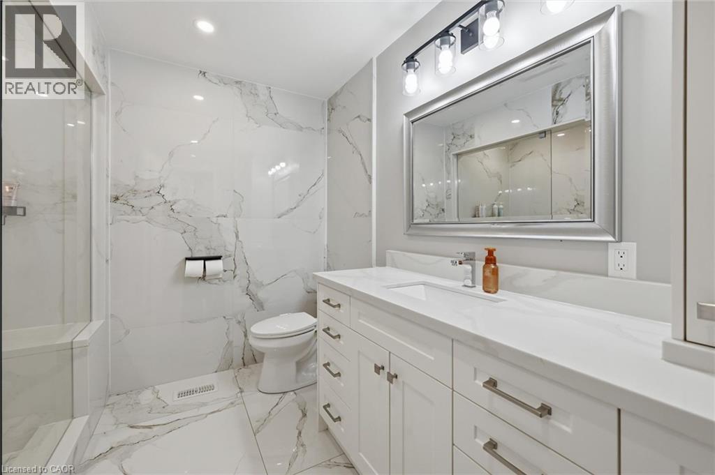 Contemporary bathroom featuring extensive marble-look tile, a frameless glass shower enclosure, and a modern vanity with a white countertop - 24 Glenwood Crescent, Hamilton, ON - Indoor Photo Showing Bathroom