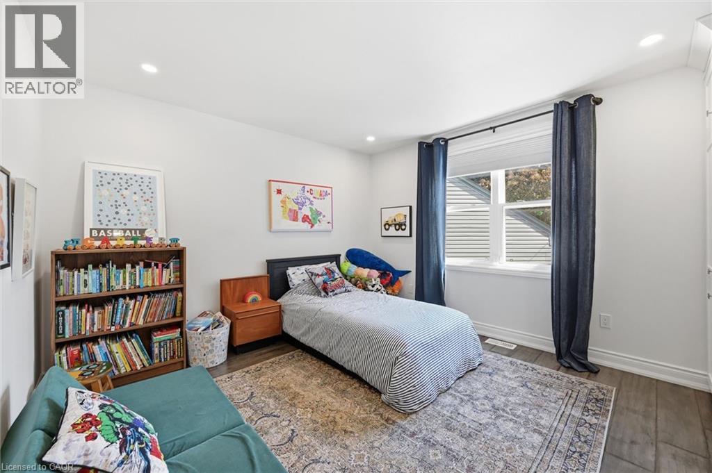 Bright interior space featuring recessed lighting, dark wood-finish flooring, white baseboards, and a window with white blinds and dark blue curtains - 24 Glenwood Crescent, Hamilton, ON - Indoor Photo Showing Bedroom