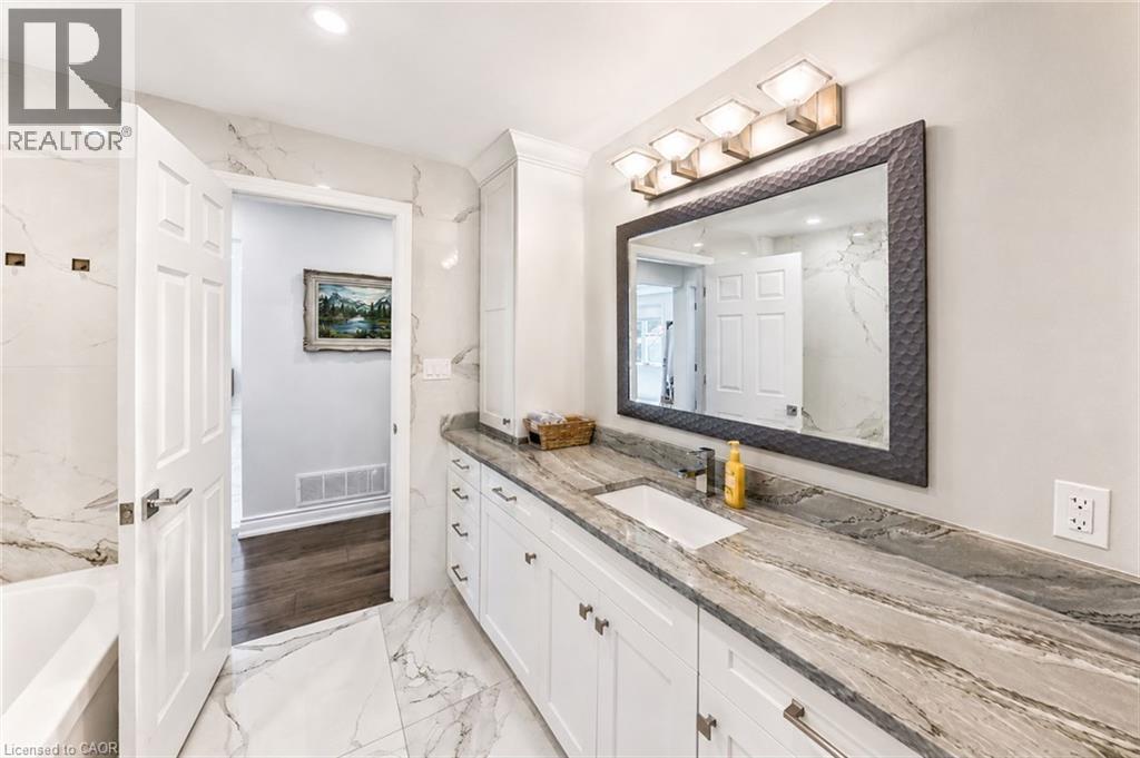 Bathroom featuring an extended vanity with dual sinks, a stone countertop, white shaker-style cabinetry, and large format marble-look tile flooring - 24 Glenwood Crescent, Hamilton, ON - Indoor Photo Showing Bathroom