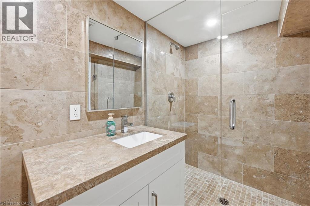 Bathroom featuring a white vanity with an integrated sink, a built-in mirror, a glass-enclosed shower, and full-height stone-look tile walls - 24 Glenwood Crescent, Hamilton, ON - Indoor Photo Showing Bathroom