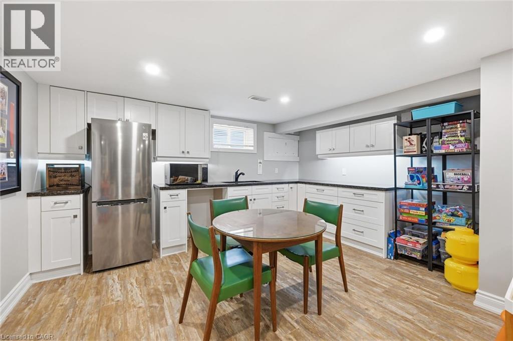 Bright kitchen area featuring white shaker-style cabinetry, dark countertops, a stainless steel refrigerator, and wood-finish flooring - 24 Glenwood Crescent, Hamilton, ON - Indoor Photo Showing Kitchen