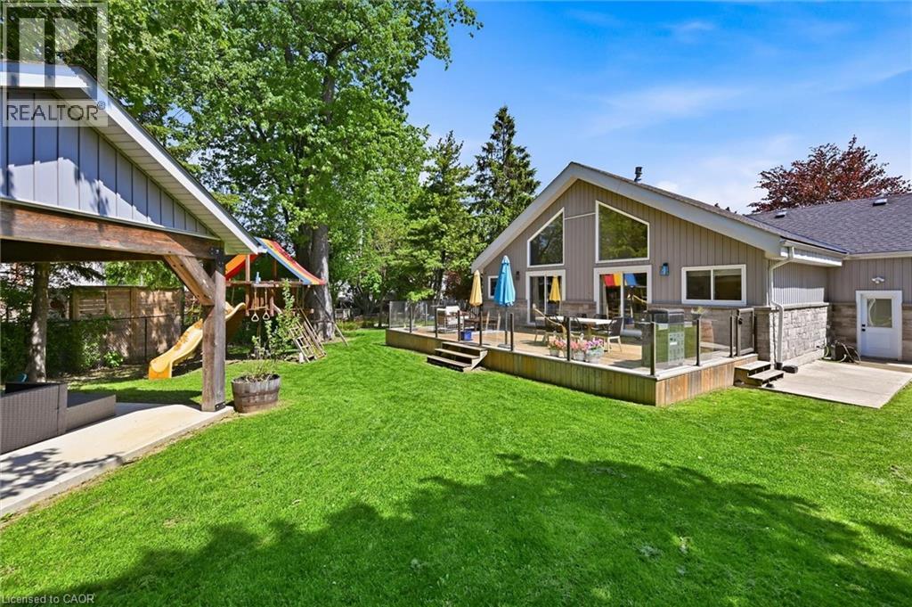 Spacious green lawn featuring a multi-level deck with glass panel railing, a covered patio area, and mature trees providing natural shade - 24 Glenwood Crescent, Hamilton, ON - Outdoor With Deck Patio Veranda