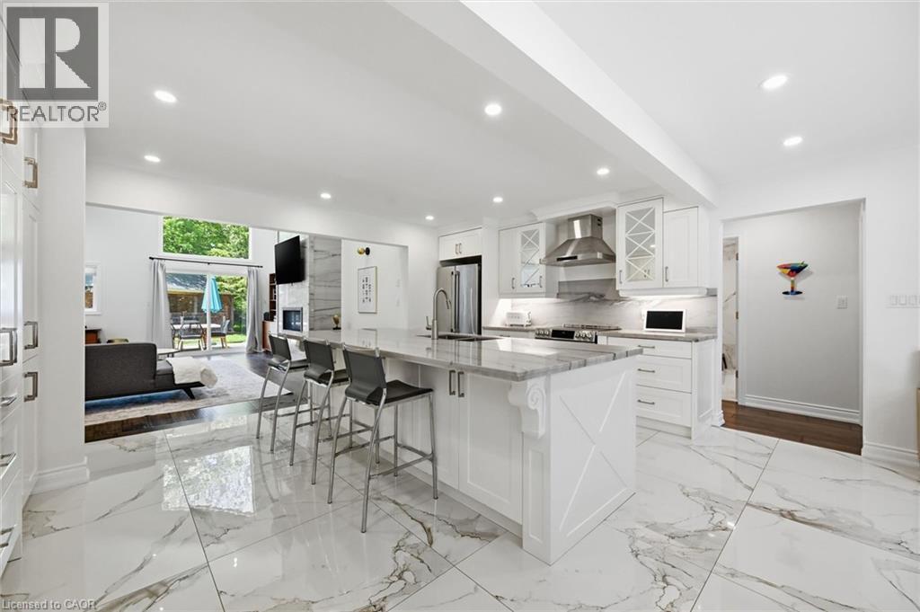 Spacious open-concept kitchen featuring a large center island with seating, white shaker cabinetry, stainless steel appliances, and marble-look tile flooring - 24 Glenwood Crescent, Hamilton, ON - Indoor Photo Showing Kitchen With Upgraded Kitchen
