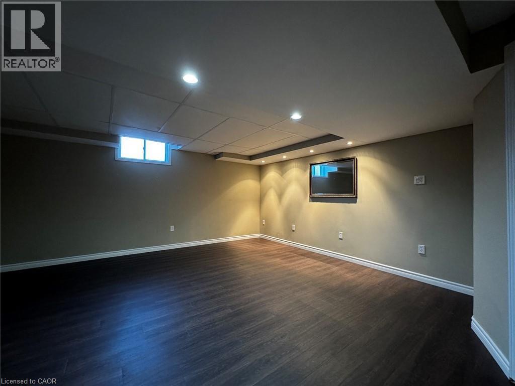 Spacious room featuring dark wood-finish flooring, light tan walls, and white baseboards - 37 Northcliffe Crescent, Cambridge, ON - Indoor Photo Showing Basement