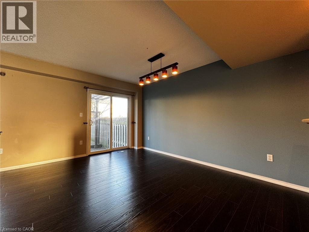 Spacious interior featuring dark wood-finish flooring, a sliding glass door leading to an outdoor deck, a modern ceiling light fixture with five individual lights, and contrasting wall colors - 37 Northcliffe Crescent, Cambridge, ON - Indoor Photo Showing Other Room
