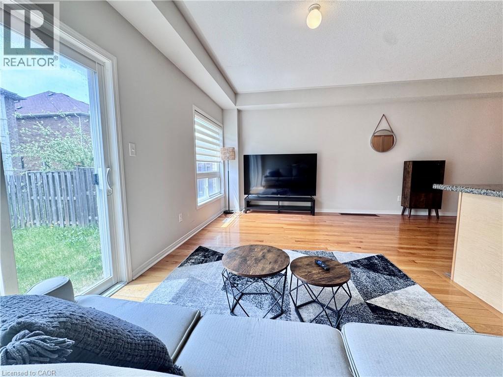 Hardwood flooring extending throughout the living space, featuring a sliding glass door to the rear yard, and a large window with horizontal blinds - 110 Highland Road E Unit# 53, Kitchener, ON - Indoor Photo Showing Living Room
