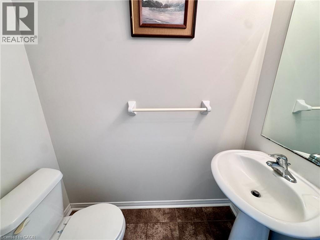 Pedestal sink with chrome faucet, a white toilet, and dark tile flooring - 110 Highland Road E Unit# 53, Kitchener, ON - Indoor Photo Showing Bathroom