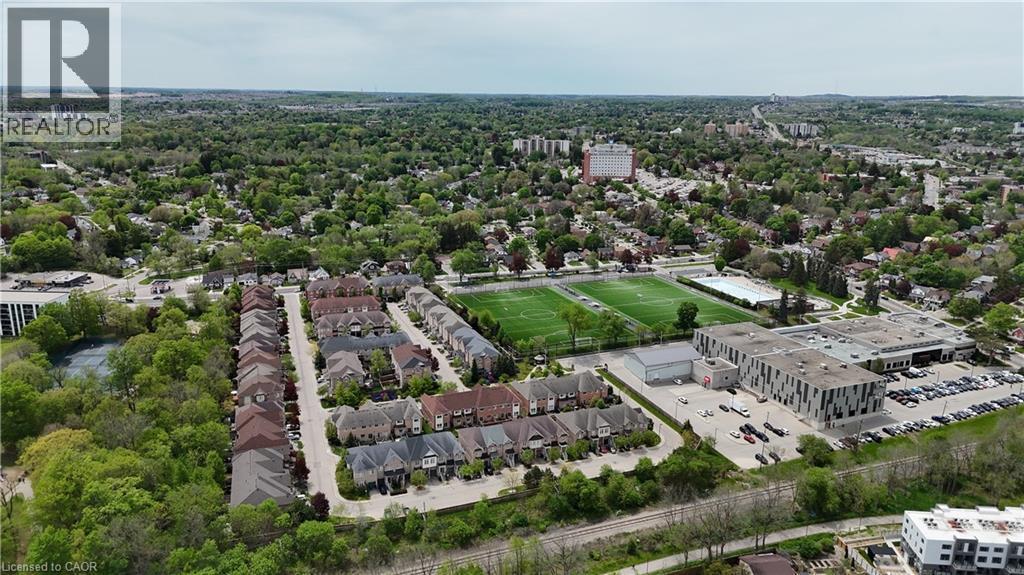 Aerial perspective showcasing a residential development surrounded by mature trees, sports fields, and a large institutional building - 110 Highland Road E Unit# 53, Kitchener, ON - Outdoor With View