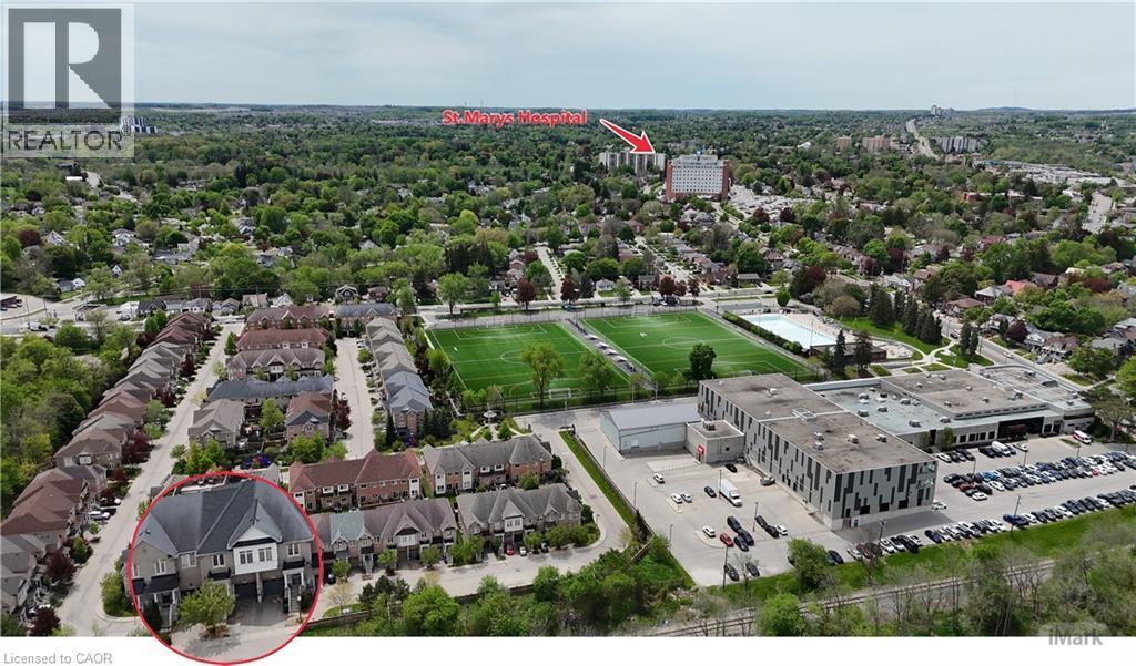 Aerial perspective showcasing a residential street with attached townhomes, positioned near a large institutional building with an expansive parking lot, and adjacent to athletic fields - 110 Highland Road E Unit# 53, Kitchener, ON - Outdoor With View