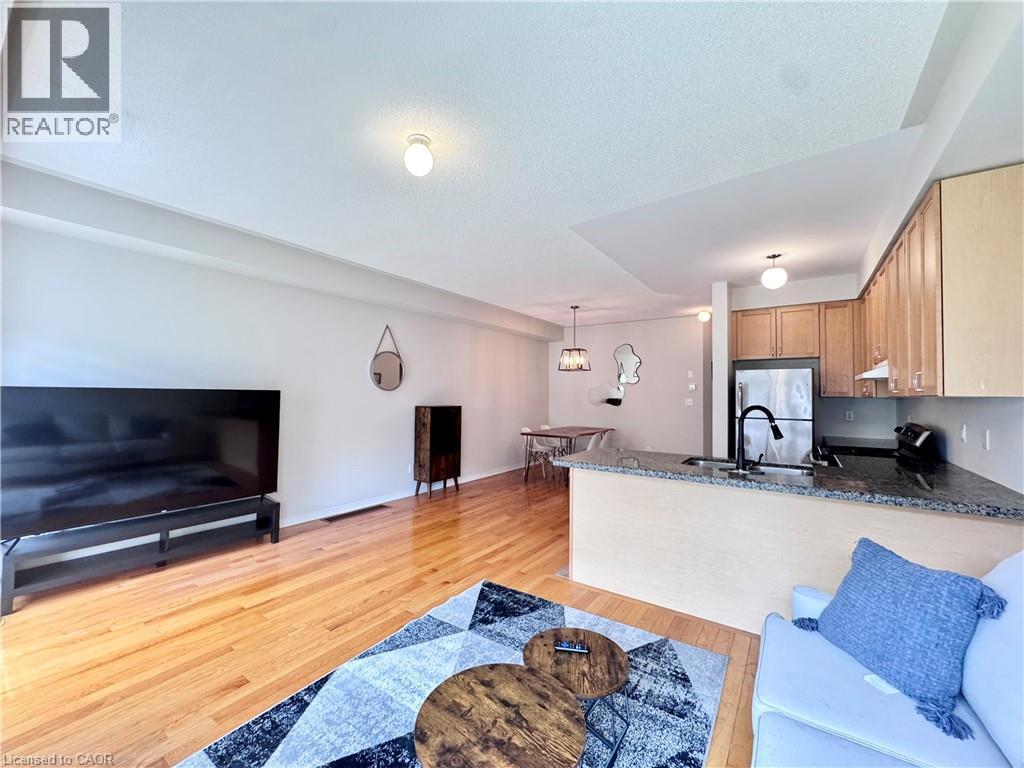 Open-concept living space featuring wood-finish flooring, a kitchen island with stone countertop, stainless steel appliances, and wood cabinetry - 110 Highland Road E Unit# 53, Kitchener, ON - Indoor