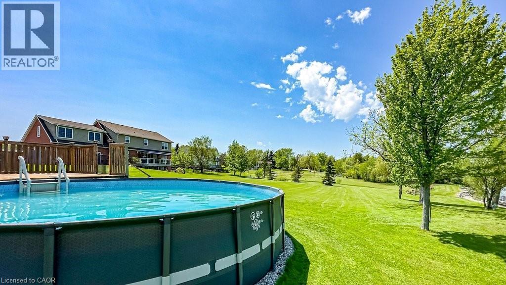 Expansive backyard featuring an above-ground pool with a surrounding wood deck, a vast lawn, and mature trees - 32A Haldimand Trail, Dunnville, ON - Outdoor With Above Ground Pool