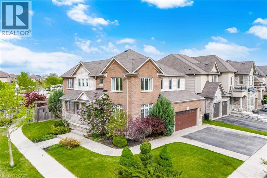 Brick and stone facade residence featuring a covered front porch, two-car garage, established landscaping, concrete driveway, and a paved walkway - 58 Doon Creek Street, Kitchener, ON - Outdoor
