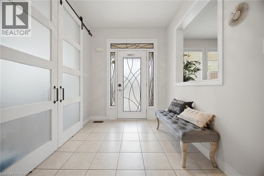 Foyer featuring tile flooring, a decorative glass entry door with sidelights, a transom window, and white barn-style sliding closet doors with frosted panels and black hardware - 58 Doon Creek Street, Kitchener, ON - Indoor Photo Showing Other Room