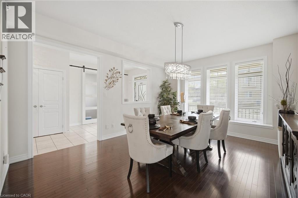 Hardwood flooring extends throughout this space, complemented by a contemporary chandelier and a wall of three windows with blinds - 58 Doon Creek Street, Kitchener, ON - Indoor Photo Showing Dining Room