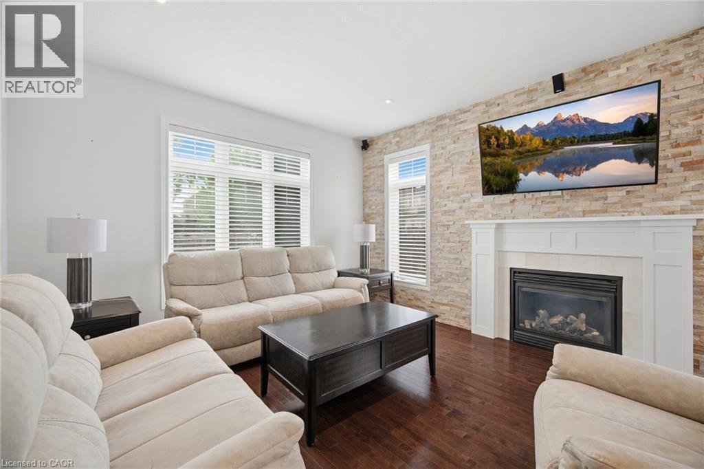Living area featuring a stone accent wall with a fireplace and white mantel, dark wood-finish flooring, and multiple windows - 58 Doon Creek Street, Kitchener, ON - Indoor Photo Showing Living Room With Fireplace