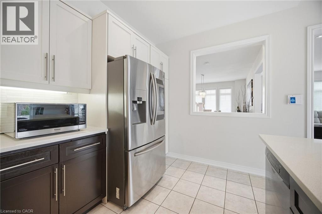 Kitchen featuring white upper cabinetry, dark lower cabinetry, and a full-size stainless steel refrigerator - 58 Doon Creek Street, Kitchener, ON - Indoor Photo Showing Kitchen