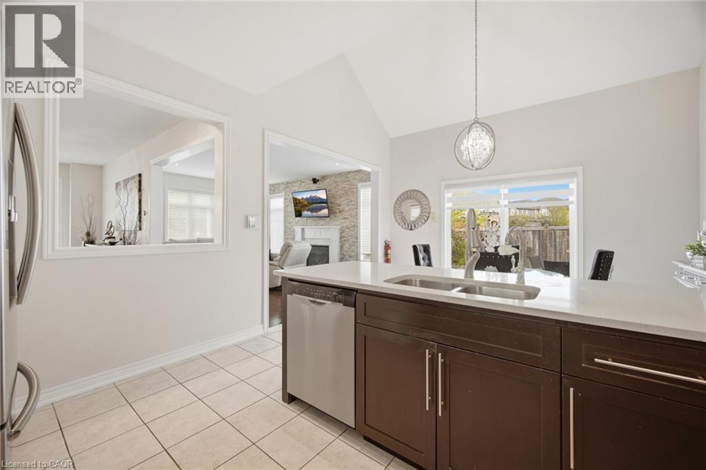 Kitchen featuring dark wood cabinetry, light-toned countertops, a double basin sink with a high-arc faucet, and stainless steel dishwasher - 58 Doon Creek Street, Kitchener, ON - Indoor Photo Showing Kitchen With Double Sink
