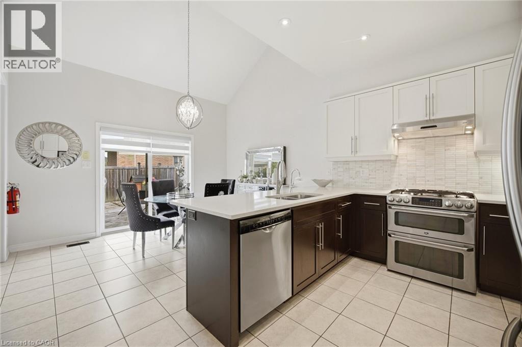 Kitchen featuring white tile flooring, two-tone cabinetry, stainless steel appliances, and a white countertop island with an undermount sink - 58 Doon Creek Street, Kitchener, ON - Indoor Photo Showing Kitchen With Upgraded Kitchen