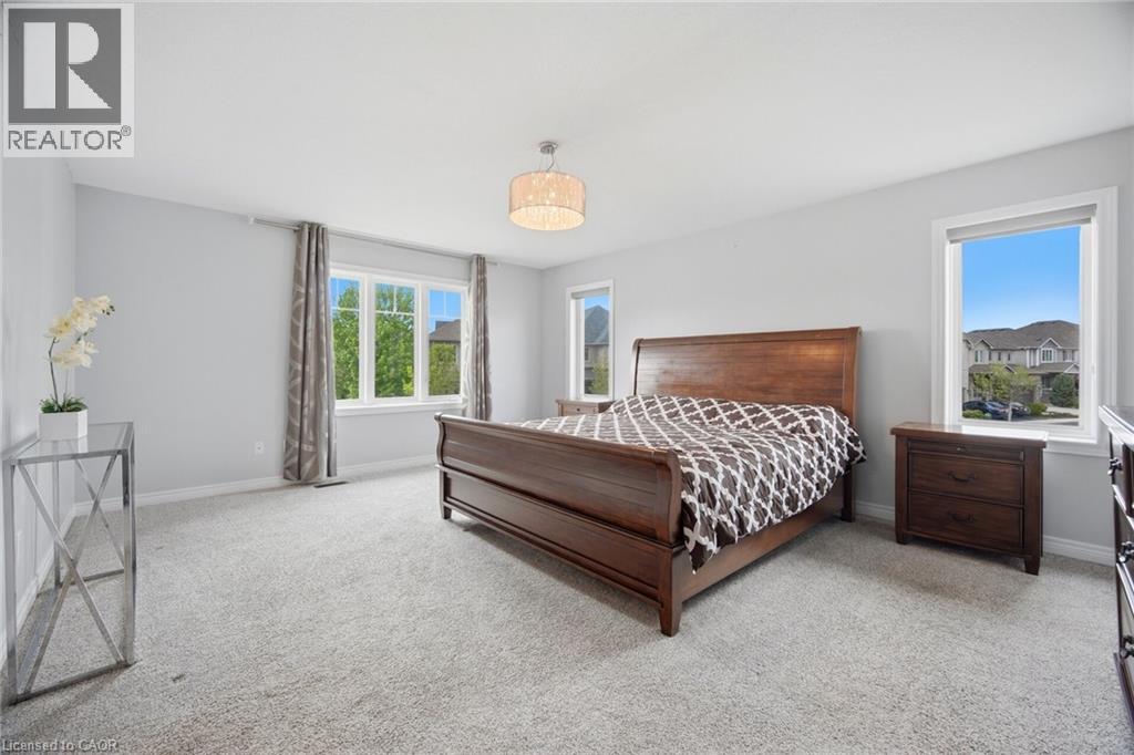Spacious room featuring light gray walls, plush carpeting, multiple windows providing ample natural light, and a contemporary ceiling light fixture - 58 Doon Creek Street, Kitchener, ON - Indoor Photo Showing Bedroom