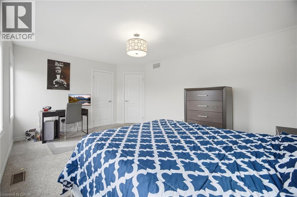 Bright room featuring light gray carpet flooring, white painted walls, two white paneled doors, and a decorative ceiling light fixture - 58 Doon Creek Street, Kitchener, ON - Indoor Photo Showing Bedroom