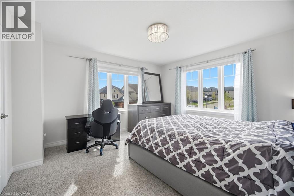 Bright room featuring a large window with multiple panes, light-colored carpeting, and a built-in ceiling light fixture - 58 Doon Creek Street, Kitchener, ON - Indoor Photo Showing Bedroom