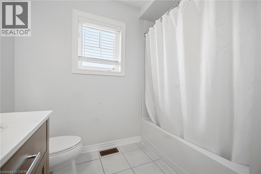 Bathroom featuring a white bathtub with shower, white tiled flooring, a window with white blinds, and a wood-finish vanity with a white countertop - 58 Doon Creek Street, Kitchener, ON - Indoor Photo Showing Bathroom