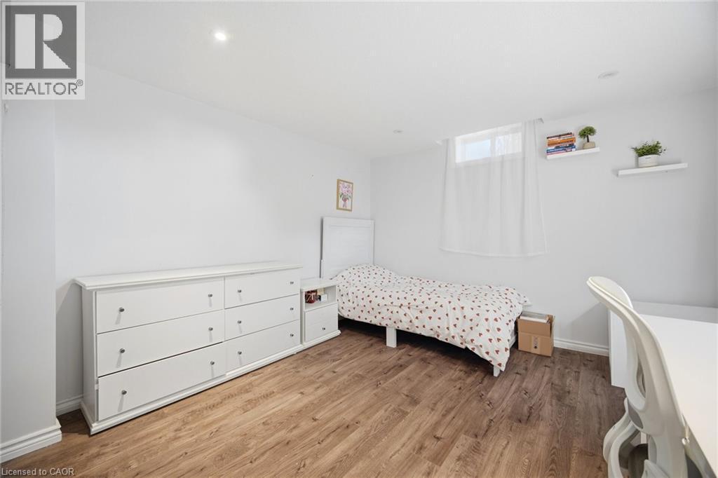 Bedroom featuring wood-finish flooring, white walls, recessed lighting, and a window with white sheer curtain - 58 Doon Creek Street, Kitchener, ON - Indoor Photo Showing Bedroom