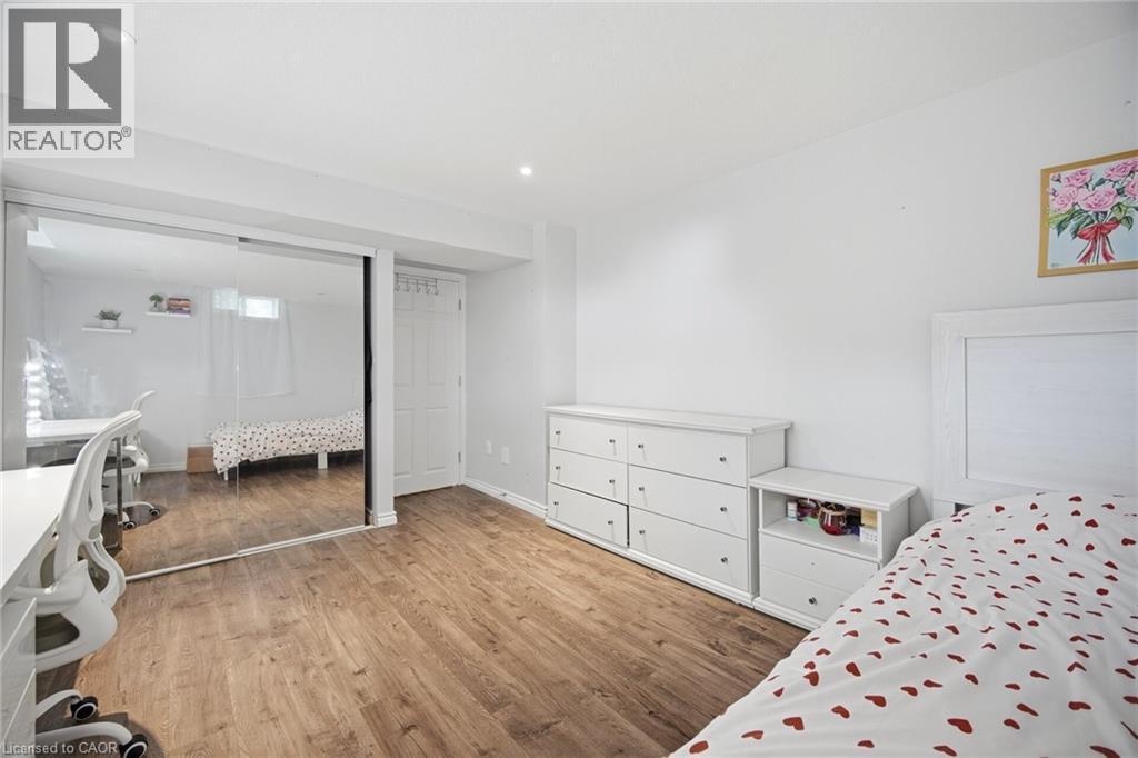 Bedroom featuring wood-finish flooring, a mirrored sliding closet door, recessed lighting, and a white paneled door - 58 Doon Creek Street, Kitchener, ON - Indoor Photo Showing Bedroom