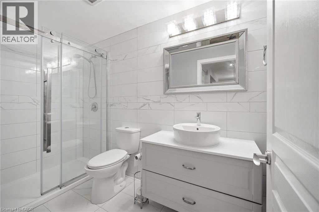 Full bathroom featuring a glass-enclosed shower, white subway-style wall tiling with a decorative accent band, and a vanity with a vessel sink and chrome hardware - 58 Doon Creek Street, Kitchener, ON - Indoor Photo Showing Bathroom