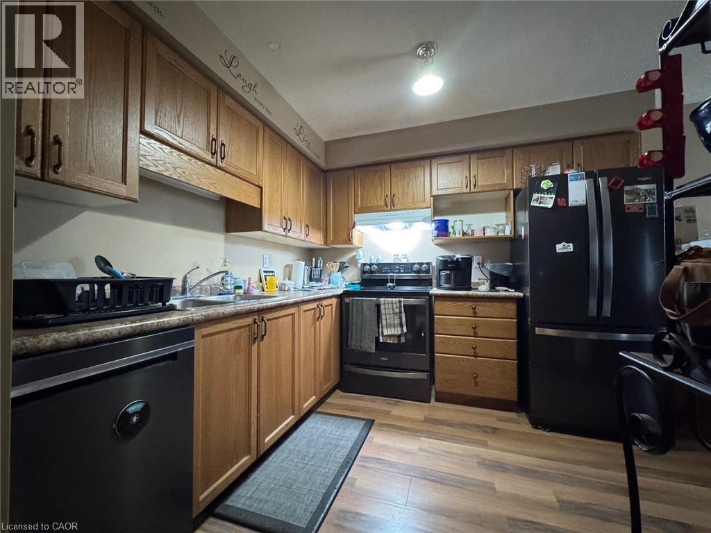 Kitchen featuring wood-finish flooring, wood cabinetry with dark hardware, a stainless steel sink, and a dark countertop - 517 Northbrook Place, Kitchener, ON - Indoor Photo Showing Kitchen With Double Sink