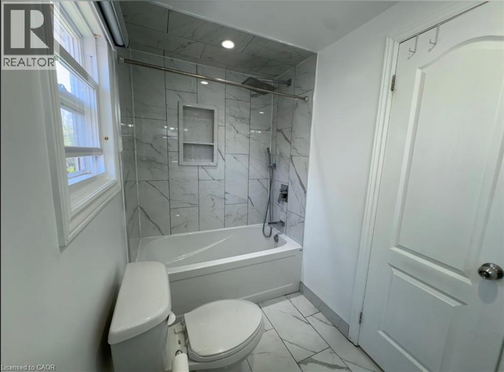 Contemporary bathroom featuring a tub/shower combination with marble-look tile surround, recessed niche, and modern fixtures - 28 Timberlane Crescent Unit# Upper, Kitchener, ON - Indoor Photo Showing Bathroom