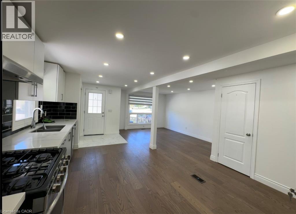 Open-concept living area featuring a modern kitchen with white cabinetry, a dark subway tile backsplash, and light-colored countertops - 28 Timberlane Crescent Unit# Upper, Kitchener, ON - Indoor Photo Showing Kitchen With Double Sink