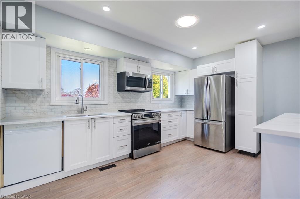 Modern kitchen featuring white shaker-style cabinetry, stainless steel appliances, a white tile backsplash, light-toned wood-finish flooring, and recessed lighting - 100 Lauris Avenue, Cambridge, ON - Indoor Photo Showing Kitchen With Upgraded Kitchen