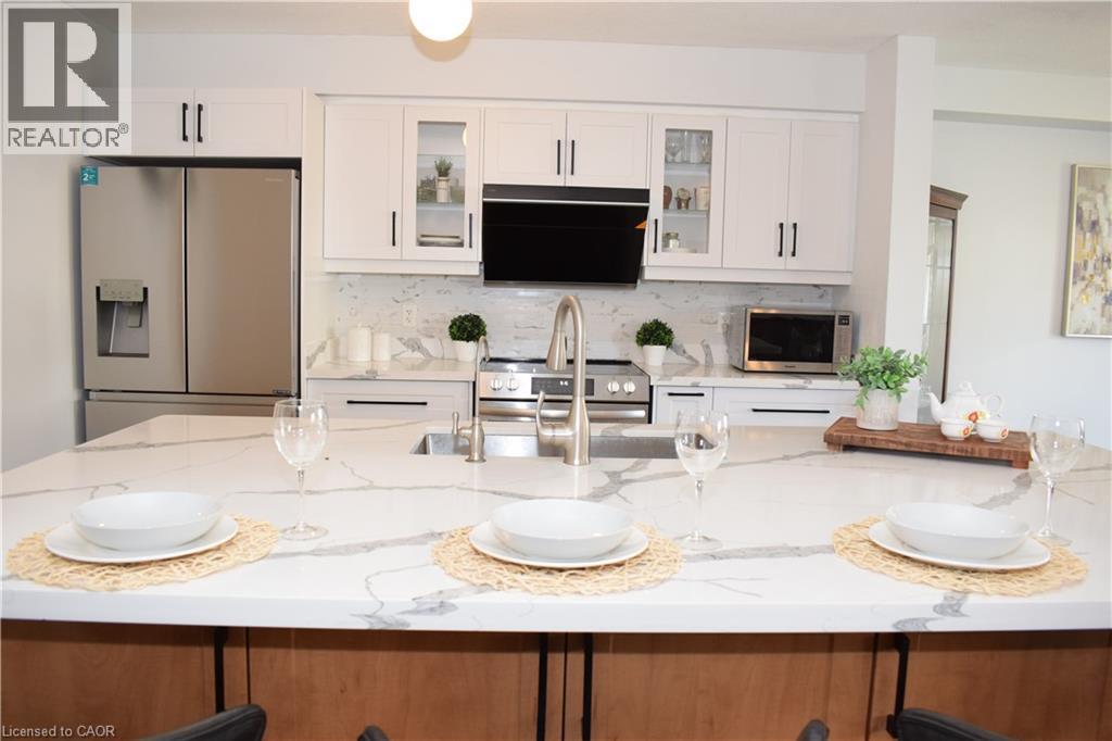 Kitchen featuring an expansive quartz island with integrated sink, stainless steel appliances, white cabinetry with black hardware, and a matching quartz backsplash - 28 Lemon Grass Street, Kitchener, ON - Indoor Photo Showing Other Room