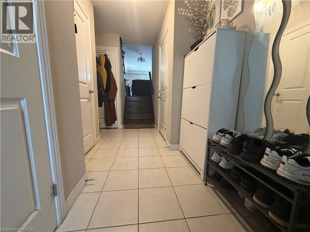 Tiled entryway with light-toned flooring extending to a staircase featuring dark wood treads - 25 Bethune Avenue, Hamilton, ON - Indoor Photo Showing Other Room