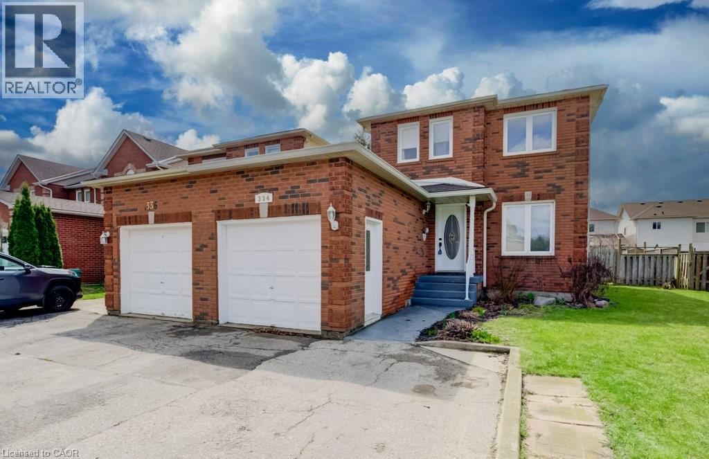 Brick exterior residence featuring a two-car garage with white doors, a concrete driveway, and a well-maintained lawn - 334 Christopher Drive, Cambridge, ON - Outdoor
