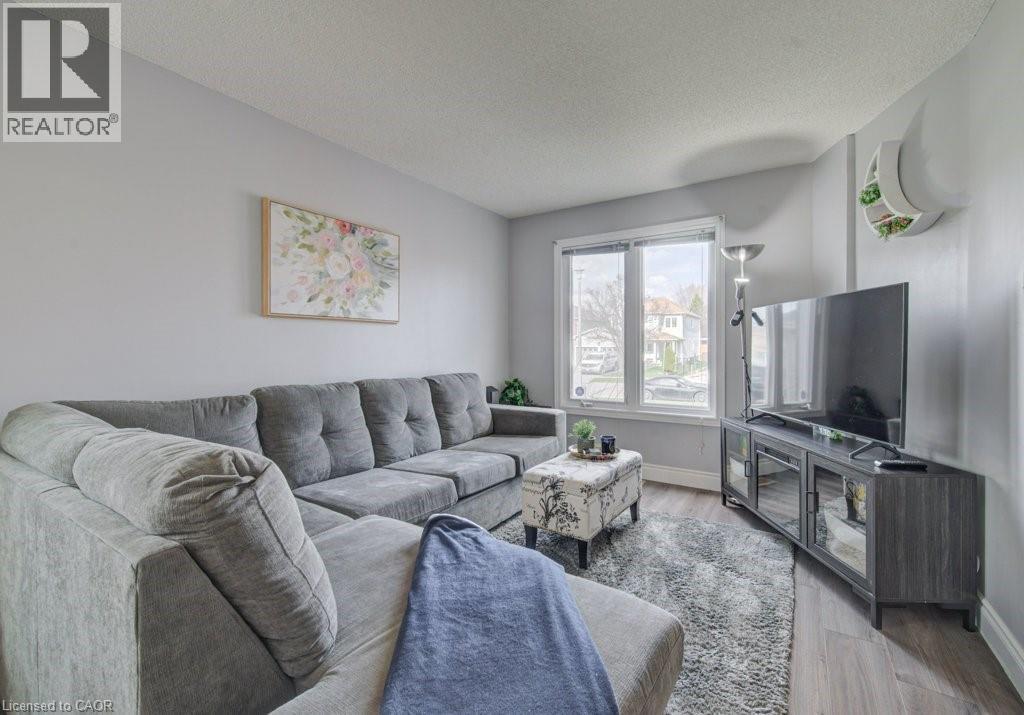 Living area featuring light grey walls, wood-finish flooring, a bright window, and a textured area rug - 334 Christopher Drive, Cambridge, ON - Indoor Photo Showing Living Room